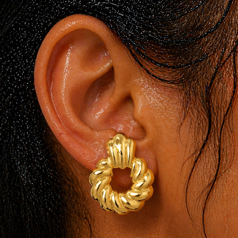 Close-up of an ear wearing a gold hoop earring with a neutral background