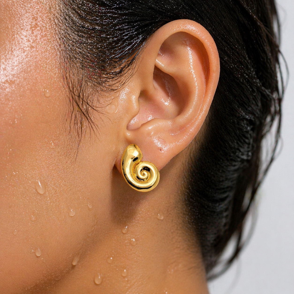 Close-up of an ear wearing a gold spiral earring with a blurred background