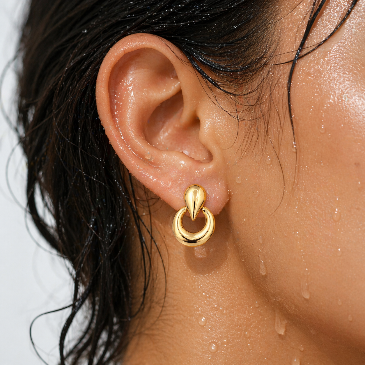 Close-up of an ear wearing a gold hoop earring with a blurred background