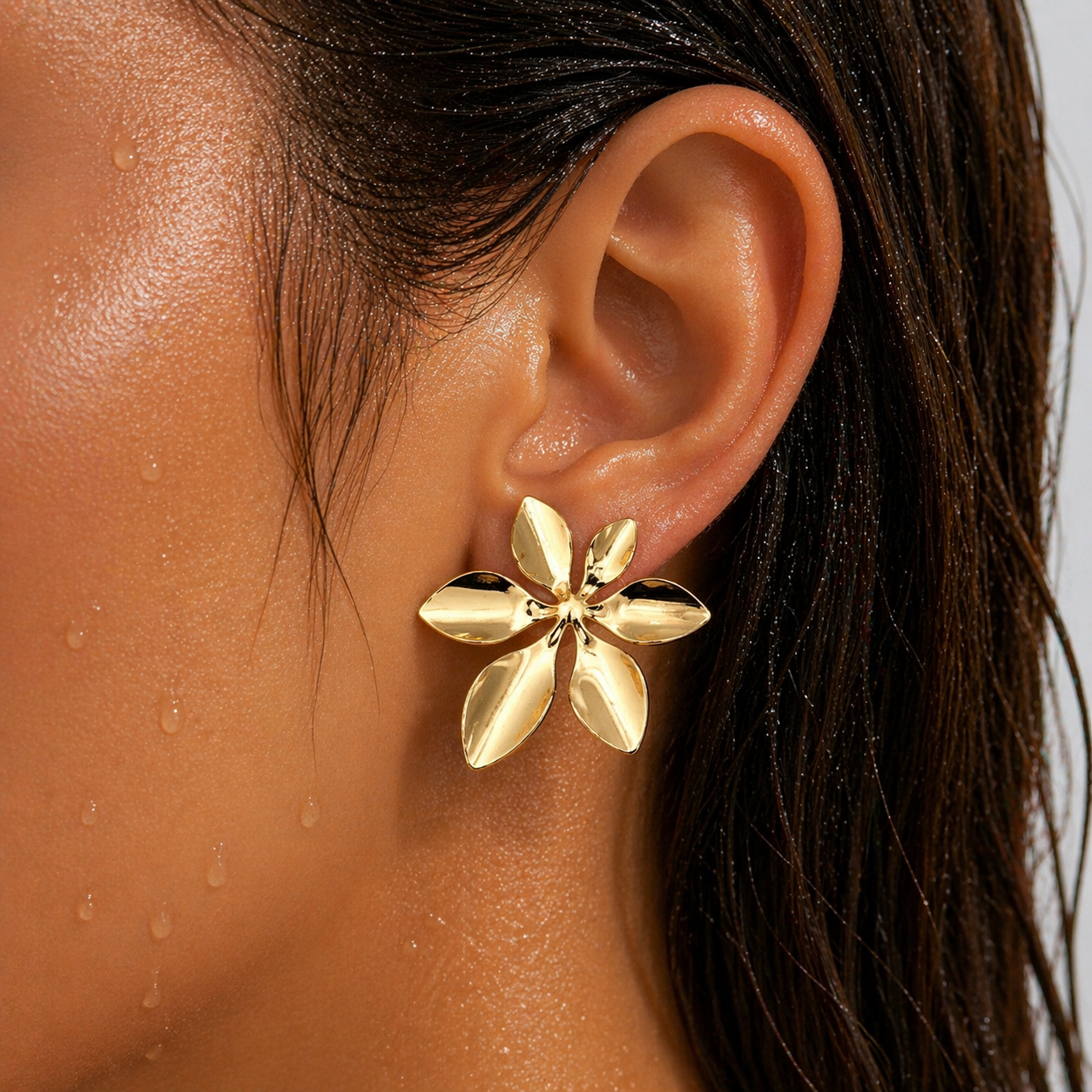 Gold flower-shaped earring worn by a person with dark hair.