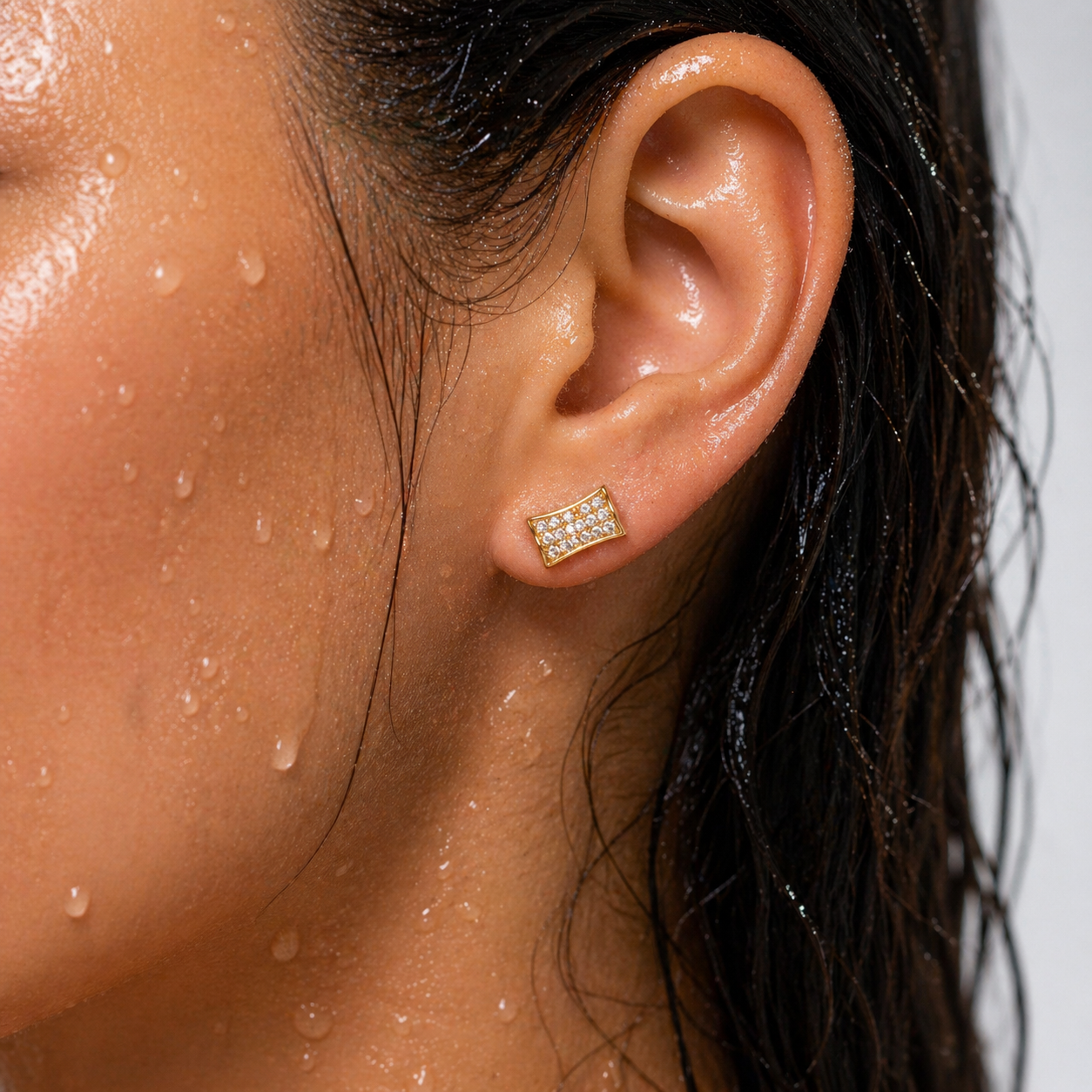 Close-up of an ear wearing a gold earring with a diamond-like stone, with skin and hair details.