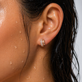 Close-up of an ear with a gold hoop earring, skin with water droplets, and dark hair.