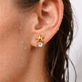 Gold star earring with a clear gemstone worn by a person.