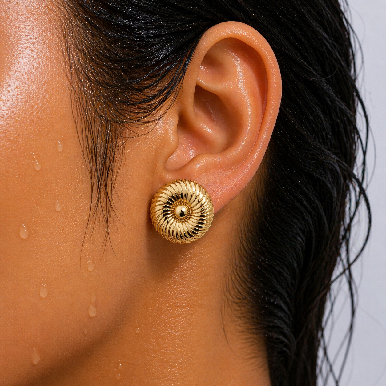 Close-up of an ear wearing a gold earring with a blurred background