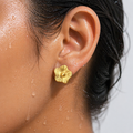 Close-up of an ear wearing a gold floral earring with a blurred background