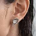 Close-up of an ear wearing a silver earring with a clear gemstone.