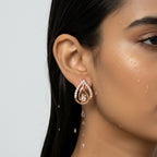 Rose gold-tone teardrop flame stud earring with pave CZ outline and center stone, close-up on model's ear