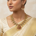 Woman wearing a gold necklace and earrings with a beige saree.