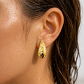 Gold-tone hammered crescent moon stud earring, close-up worn on ear showing textured finish