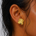 Gold textured earring worn by a person with dark hair.