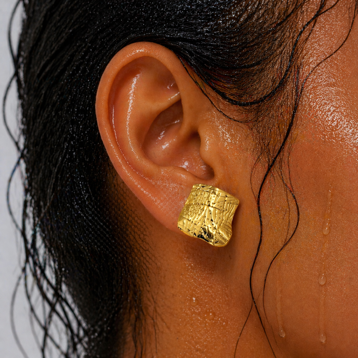 Gold textured earring worn by a person with dark hair.