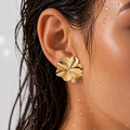 Close-up of an ear wearing a gold floral earring with a blurred background