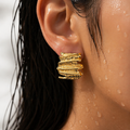 Close-up of a gold earring worn by a person with water droplets on skin and hair.