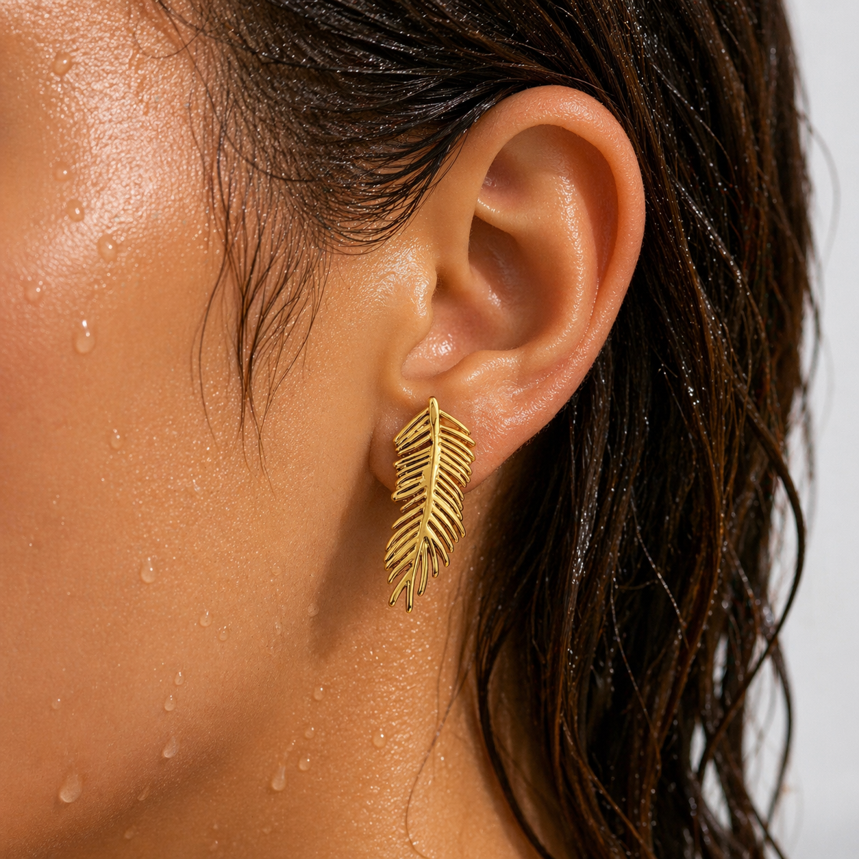 Close-up of an ear wearing a gold feather-shaped earring with a blurred background