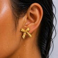 Gold bow-shaped earring worn by a person with wet skin.