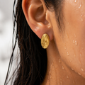 Close-up of an ear wearing a gold earring with water droplets on skin