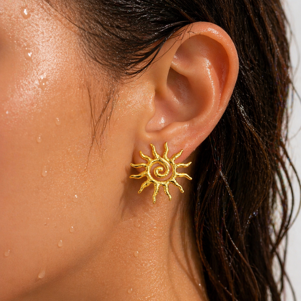 Close-up of an ear wearing a gold sun-shaped earring with a blurred background.
