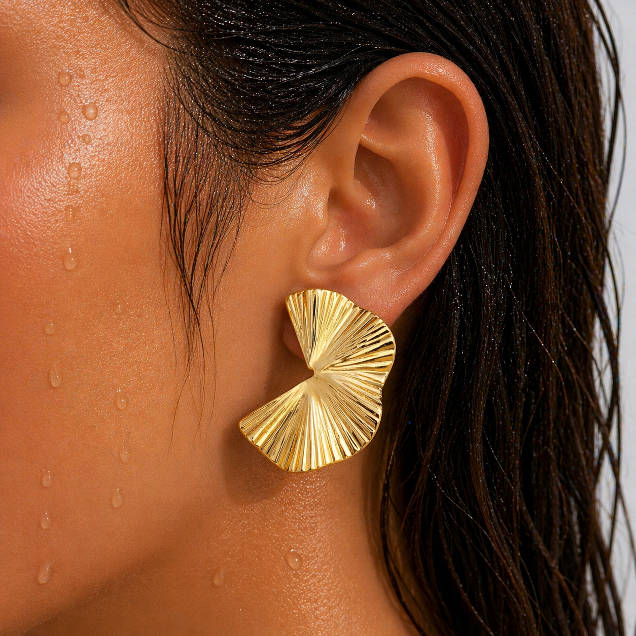 Close-up of a person wearing a gold earring with water droplets on skin