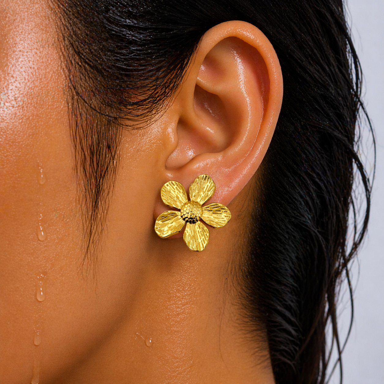 Gold flower earring worn by a person with dark hair.
