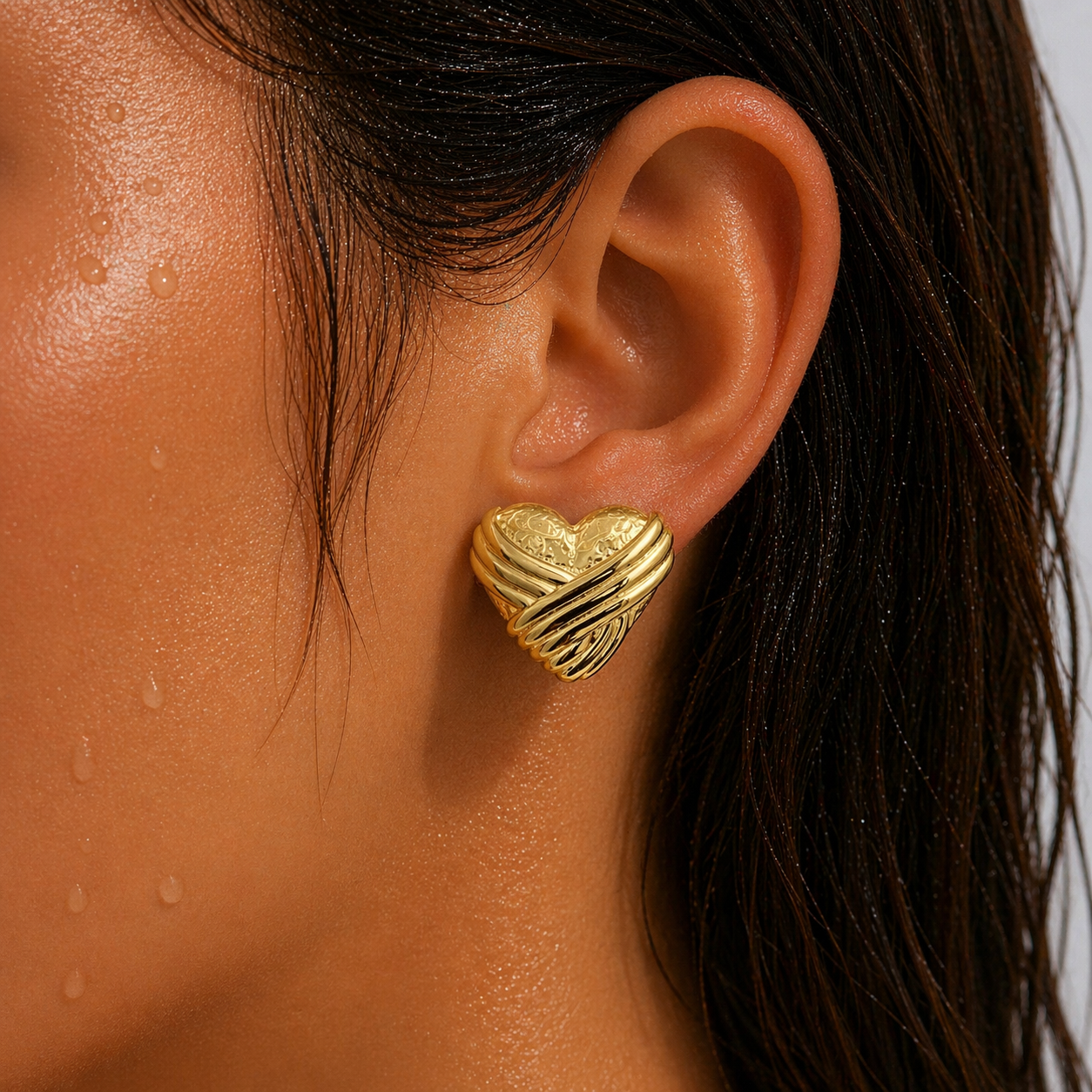 Close-up of an ear wearing a gold heart-shaped earring with a blurred background