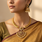 Woman wearing gold jewelry including a necklace and earrings on a neutral background