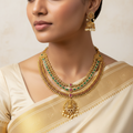 Woman wearing a gold necklace and earrings with a beige saree.