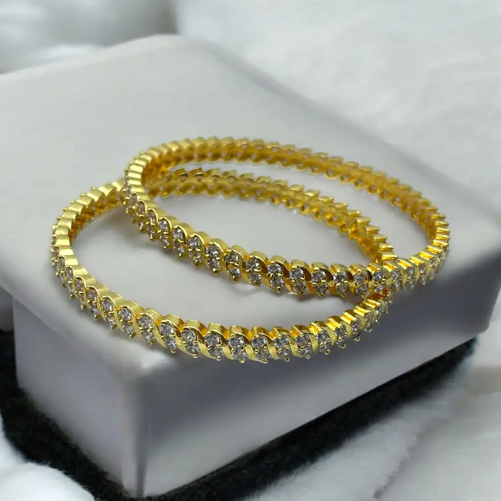 Gold-plated crystal bangle pair with wave-set stones, flat-lay on white jewellery box