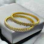 Gold-plated crystal bangle pair with wave-set stones, flat-lay on white jewellery box