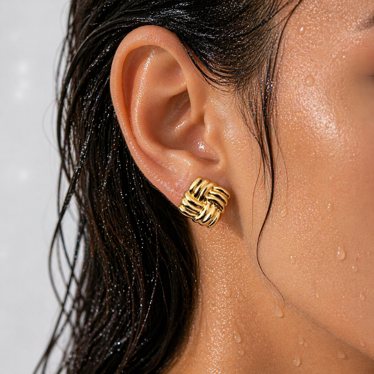 Close-up of an ear wearing a gold knot earring with a blurred background