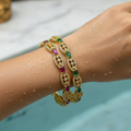 Gold-plated bangle set with ruby-red and emerald-green stones, worn stacked on wrist with water droplets