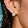 Close-up of an ear wearing a pearl earring with water droplets on skin and hair.