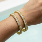 Gold bangle set with baguette crystals, pair worn stacked on wrist with water droplets