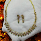 Gold-plated floral crystal necklace and drop earrings set with ruby and green accents, flat-lay on white fabric