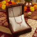 Necklace in a wooden box with decorative flowers and a lit candle in the background