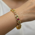 Gold-plated crystal bangle with ruby and emerald stones worn on wrist, water droplets showing waterproof finish