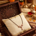 Necklace on a white pillow in a wooden box with decorative flowers and items in the background