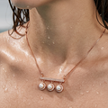 Close-up of a necklace with pearl pendants on a person with water droplets on their skin.