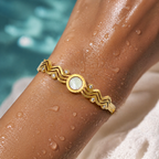 Gold bracelet with a central stone on a wet arm by a pool