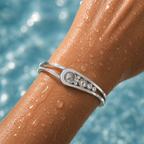 Silver bracelet with gemstones on a wet arm against a blurred water background
