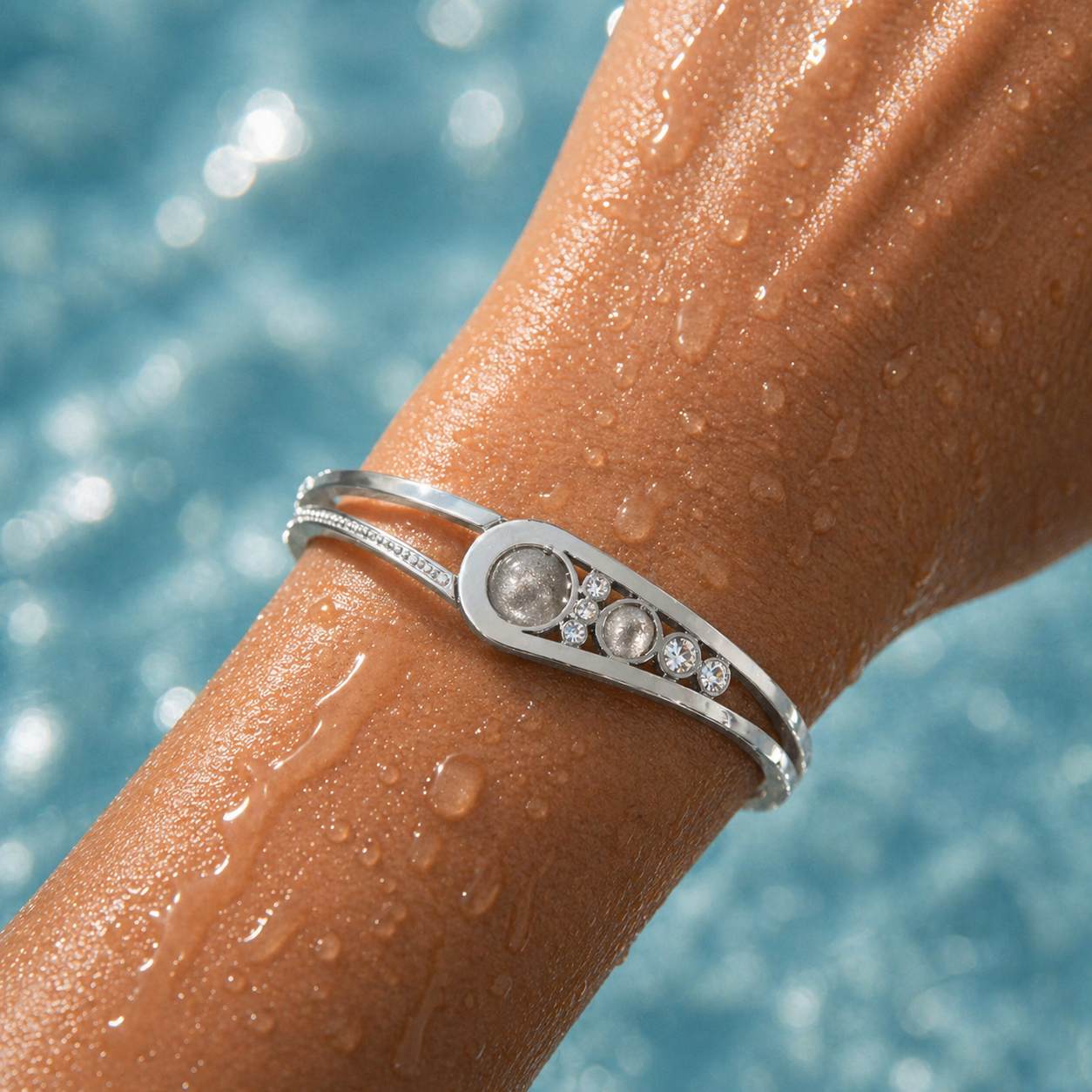 Silver bracelet with gemstones on a wet arm against a blurred water background