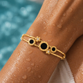 Gold bracelet with black stones on a person's wrist by a pool.