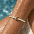 Gold bracelet with clear stones on a wet arm by a pool