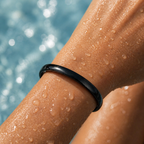 Close-up of a person's arm with water droplets wearing a black bracelet by a pool.