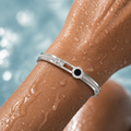 Silver bracelet with a black gemstone on a wet arm against a blurred water background