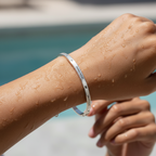 Person's arm with a silver bracelet by a pool
