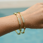 Gold-plated crystal bar bangle set with emerald and ruby-tone stones, worn on a water-splashed wrist