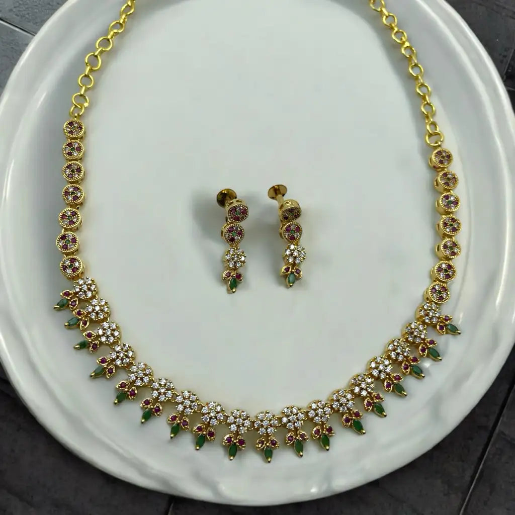 Gold-plated floral necklace and earrings set with crystal, ruby and green accents, worn by model in a gold saree